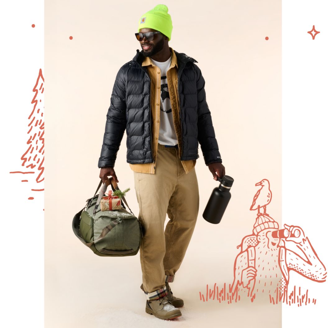A man wearing a Carhartt beanie, black puffy jacket, and hiking boots carries a duffel bag, a Hydro Flask, and a wrapped gift.  